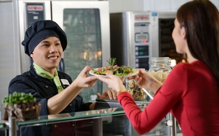 Frau bekommt an SB-Theke einen Salat gereicht.