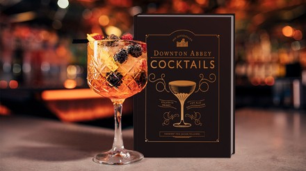 Das Buch „Die offiziellen Downton Abbey Cocktails“ steht neben einem gefüllten Cocktailglas