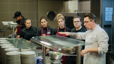 Ein Koch erklärt Auszubildenden in einer Küche die Abläufe