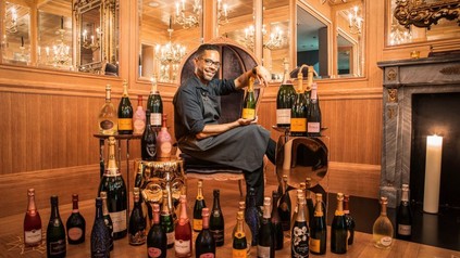 Luis Pereira Castillo sitzt zwischen Champagnerflaschen