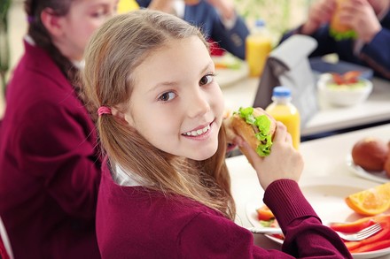 ein Kind in einer Kantine mit einem gesunden Brötchen in der Hand
