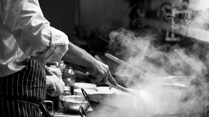 Nahaufnahme eines Kochs, der am Herd steht und in Töpfen rührt