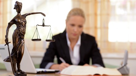 Anwältin sitzt am Schreibtisch, Statue Justita im Vordergrund