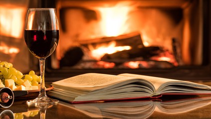 Ein Glas Wein und ein aufgeschlagenes Buch vor einem offenen Kamin