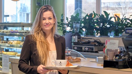 Junge Frau in einem Coffeeshop mit einem Tablett in der Hand, auf dem eine Kaffeetasse steht