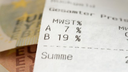 Nahaufnahme eines Kassenbons mit Blick auf die Mehrwertsteuer, im Hintergrund liegen Euro-Geldscheine
