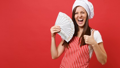 Frau mit Kochmütze hält Geldscheine in der Hand