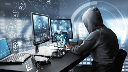 Ein Mann mit Kapuze sitzt an einem PC, um Daten zu stehlen