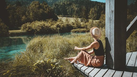 Junge Frau sitzt auf der Veranda einer Hütte in der unberührten Natur