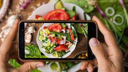 Eine Frau macht ein Handyfoto von einem veganen Essen