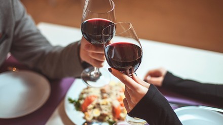 Nahaufnahme von zwei jungen Menschen, die im Restaurant sitzen und mit Weingläsern anstoßen