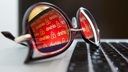 Eine Brille auf einer PC-Tatstatur, in deren Gläsern sich der Schriftzug von "Airbnb" spiegelt