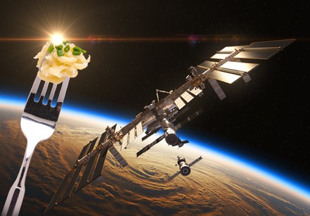 Die Internationale Raumstation von außen und eine Gabel mit Spätzle im Vordergrund