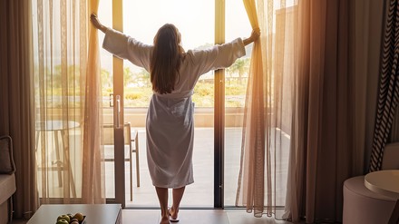Frau im Bademantel öffnet Vorhänge an der Tür eines Hotelzimmers