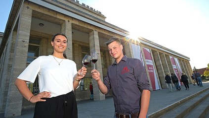 Zwei junge menschen prosten sich auf vor einem Berliner Gebäude mit Weingläsern zu