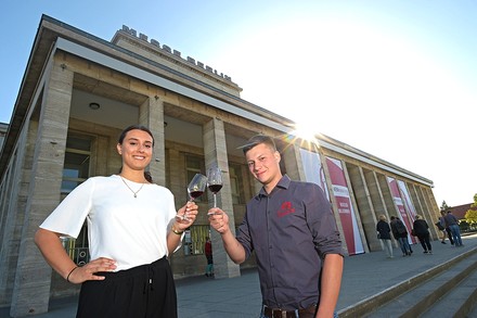 Zwei junge menschen prosten sich auf vor einem Berliner Gebäude mit Weingläsern zu