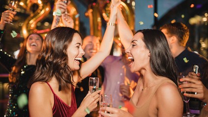 Zwei Frauen lachend mit Sektglas in der Hand auf einer Party