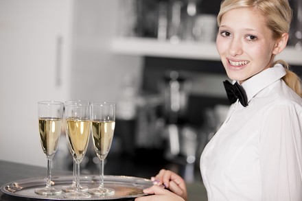 Eine lächelnde Servicekraft mit einem Tablett Sektgläser in der Hand