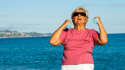 Seniorin mit Hanteln am Strand
