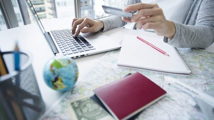 Eine Person tippt an einem Laptop und hält in der anderen Hand eine Bankkarte