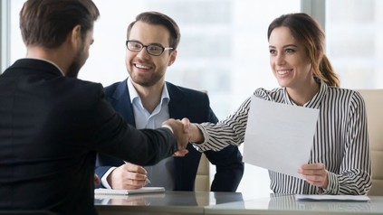 Mitarbeiter einer Firma begrüßen sich sitzend an einem Schreibtisch