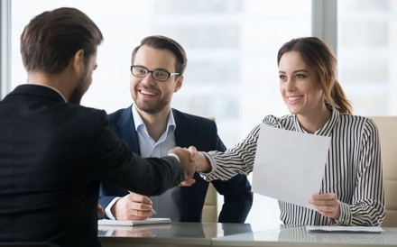 Mitarbeiter einer Firma begrüßen sich sitzend an einem Schreibtisch