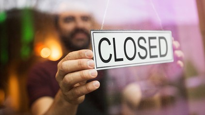 Ein Mann hängt ein Geschlossen-Schild in die Glastür eines Restaurants oder einer Bar