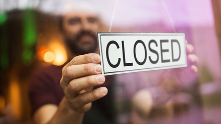 Ein Mann hängt ein Geschlossen-Schild in die Glastür eines Restaurants oder einer Bar