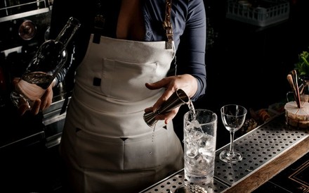 Barkeeper schenkt eine klare Spirituose in ein mit Eis gefülltes Glas