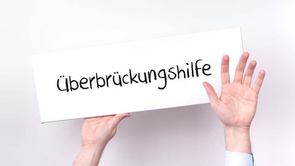Hände halten ein Schild mit der Aufschrift "Überbrückungshilfe" hoch