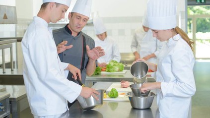 Koch in Küche erklärt Azubis etwas