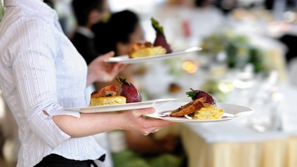 Kellnerin trägt mehrere volle Teller an einen Tisch