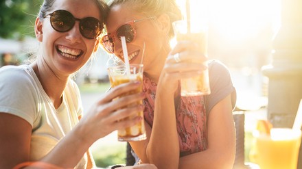Zwei Frauen sitzen lachend mit ihren Getränken im Café