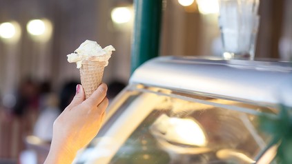 Nahaufnahme einer Hand eines Mädchens, das eine Eiswaffel mit einer Kugel Eis in einer Eisdiele entgegenimmt