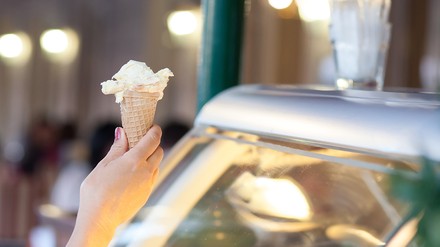Nahaufnahme einer Hand eines Mädchens, das eine Eiswaffel mit einer Kugel Eis in einer Eisdiele entgegenimmt