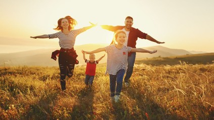 Glückliche Familie läuft im Sonnenuntergang über ein Feld