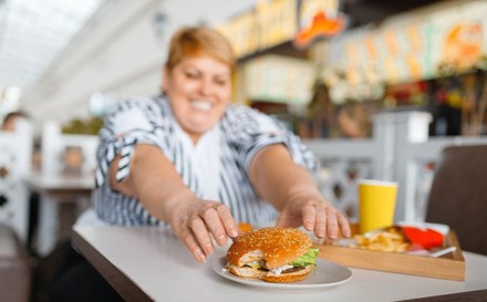 Dicke Frau greift nach angebissenem Burger