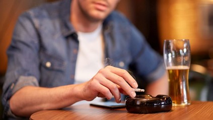 Ein Mann sitzt beim Biertrinken an einem Tisch und raucht eine Zigarette