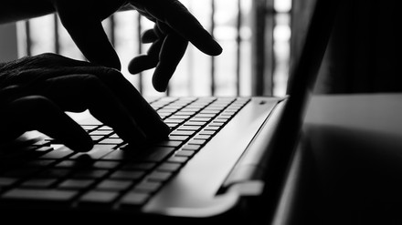 Nahaufnahme in Schwarz-Weiß von Händen, die etwas in einen Laptop tippen; Hacker-Angriff