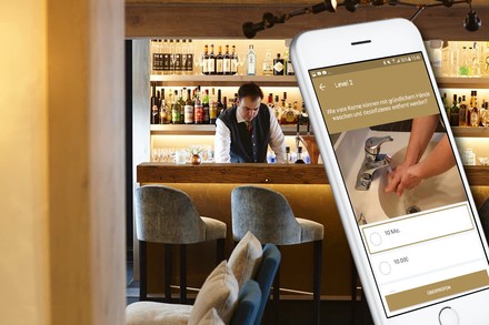 Ein Barkeeper im Hintergrund, ein Handy mit Lern-App im Vordergrund