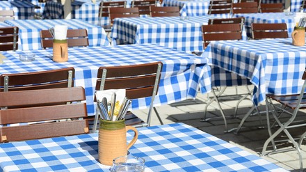 Tische in einem bayerischen Biergarten mit blau-weiß-kariertem Tischtuch und Besteck