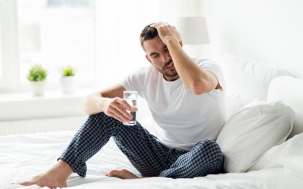 Verkaterter Mann im Bett mit einem Glas Wasser