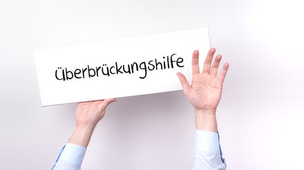 Hände halten Schild mit der Aufschrift „Überbrückungshilfe“