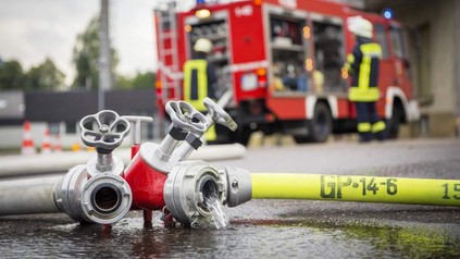 Feuerwehrschlauch mit Feuerwehrwagen im Hintergrund